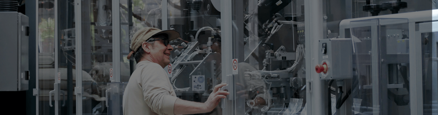 Worker operating or inspecting industrial machinery behind a glass enclosure in a modern manufacturing or production facility.