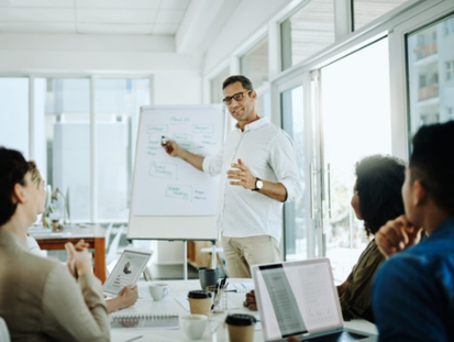 man in office meeting setting pointing at a whiteboard