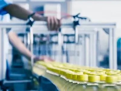 Close-up of a production line in a factory, with plastic bottles moving along a conveyor belt and a worker operating machinery.