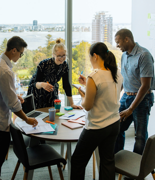 four people around a desk talking in an office setting