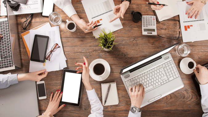 Image of busy professionals working with their laptops and drinking coffee around a table. 