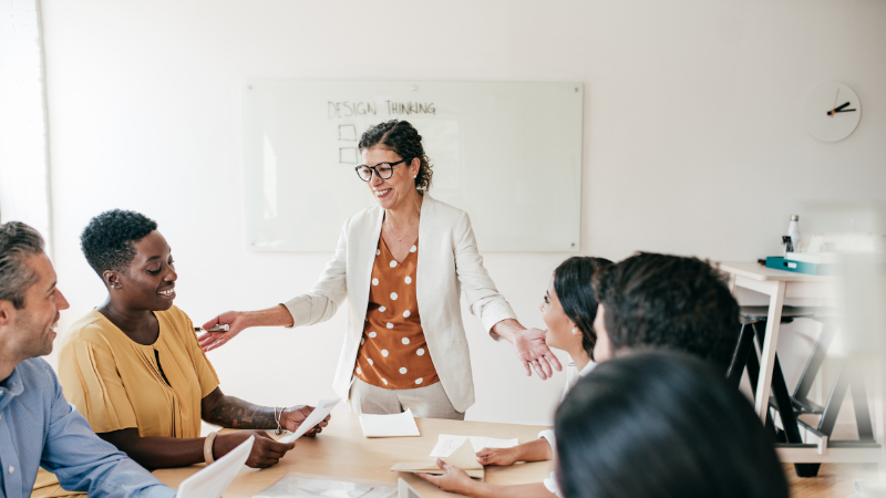 female leader standing up around a table and turned towards her team of 5