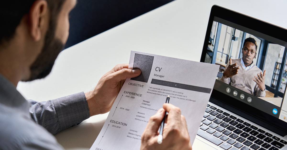 Man looking at CV while interviewing someone on his laptop